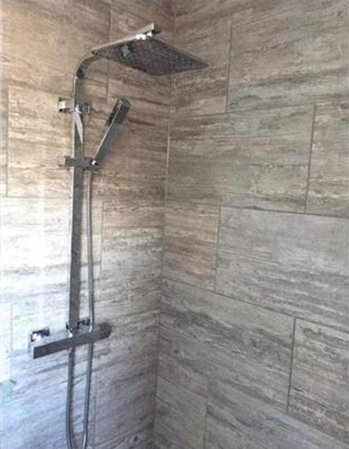A shower with a chrome rain head on grey tiling
