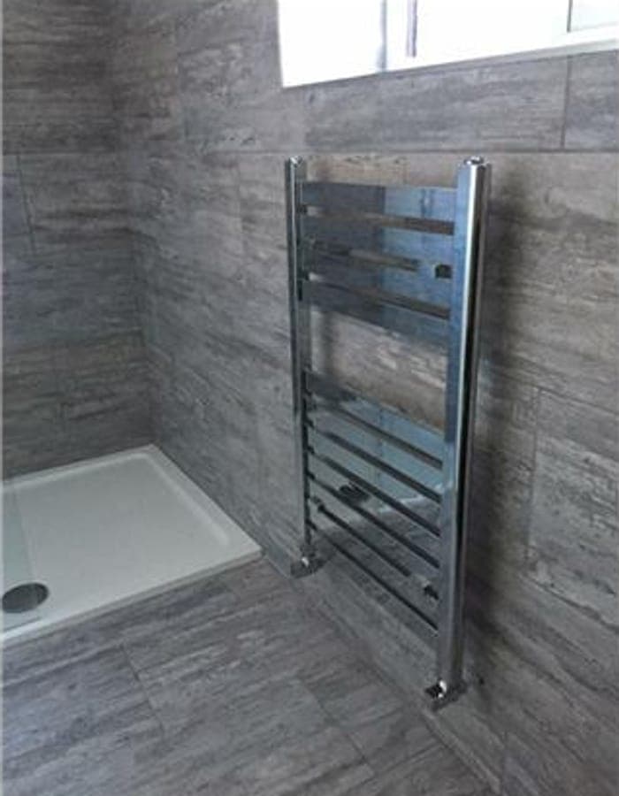 A shower tray and chrome towel rail in a tiled shower room