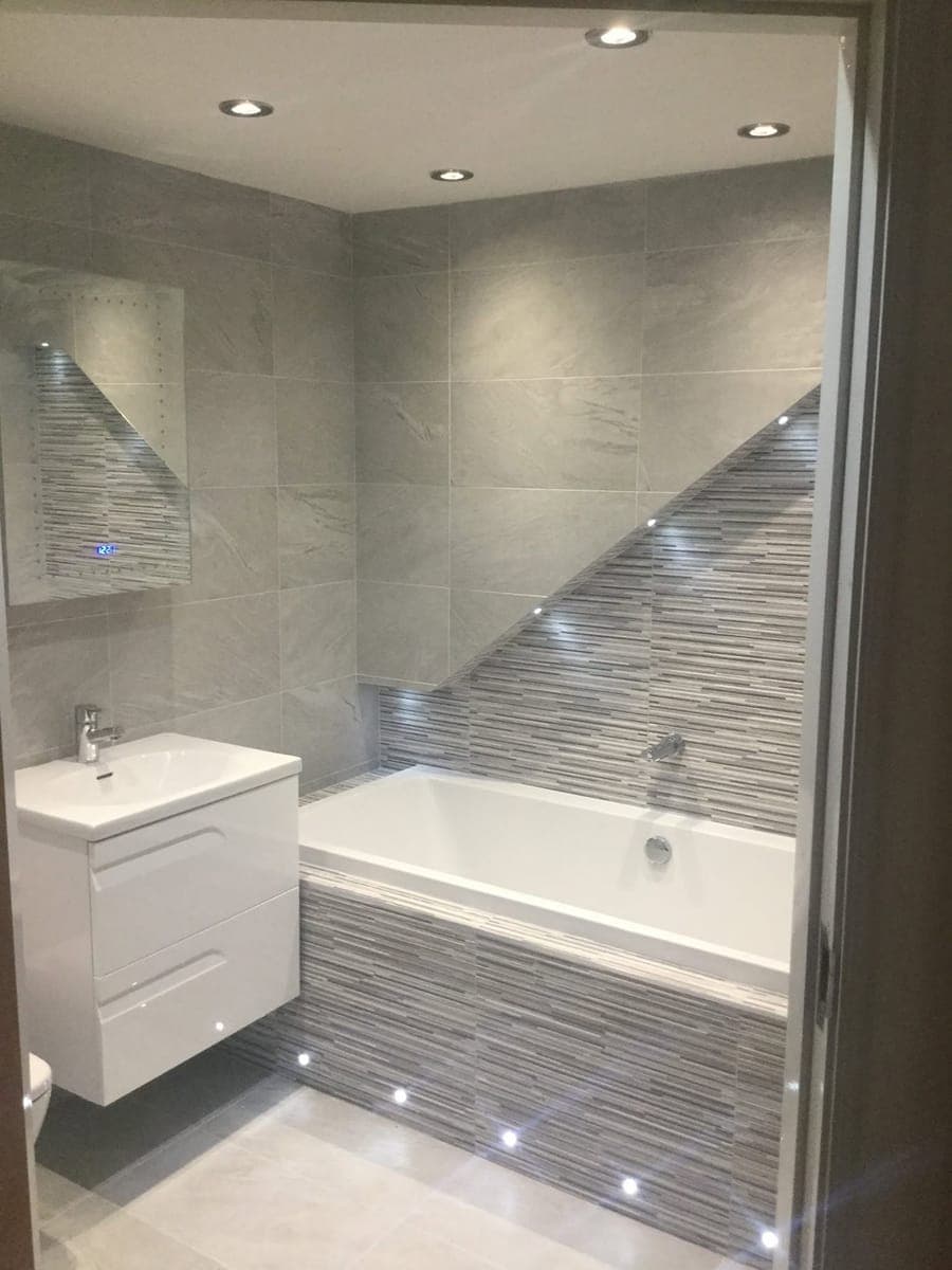 A grey stone tiled bathroom with a linear mosaic feature wall and LED floor lighting
