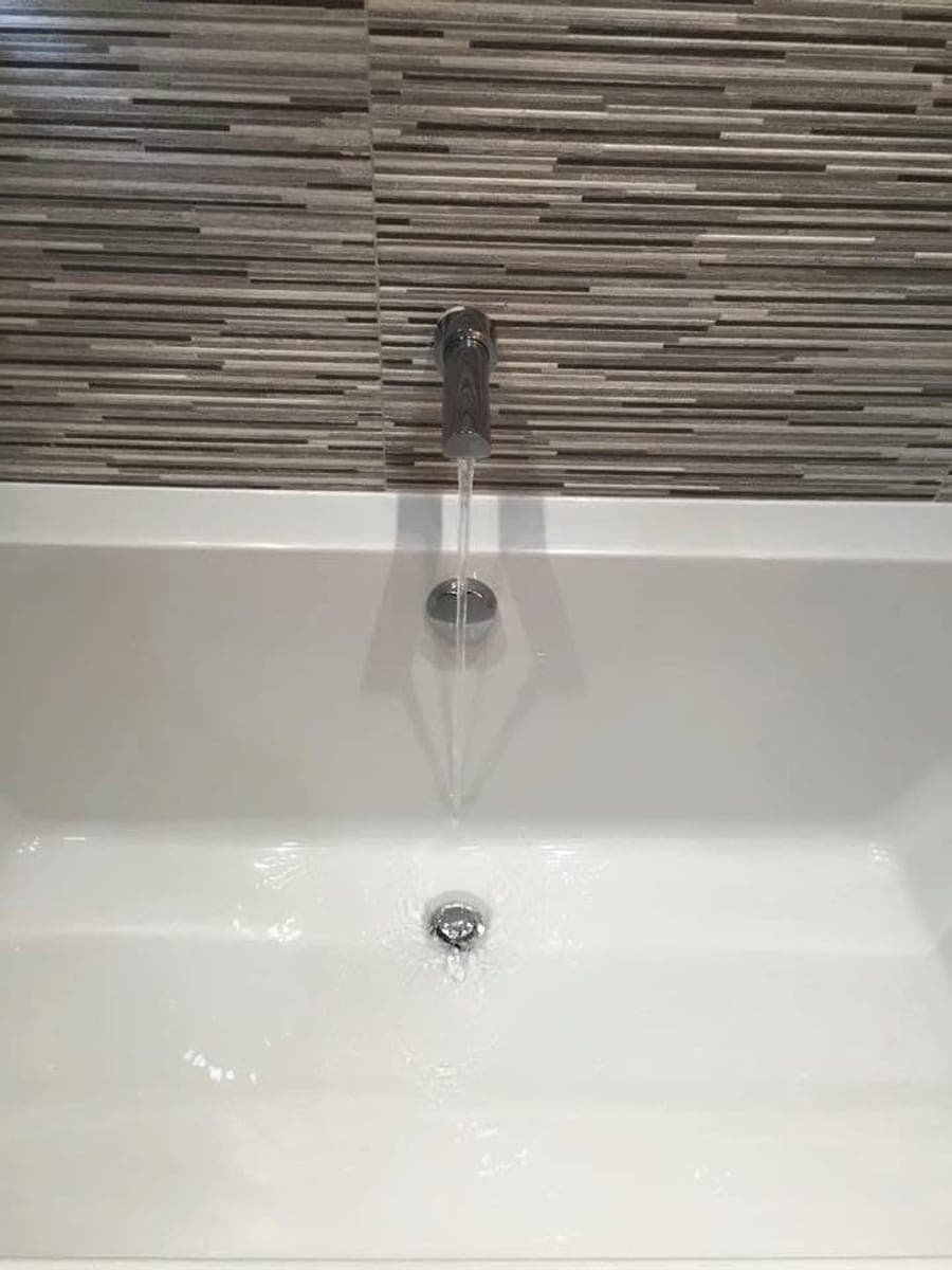 A wall mounted bath filler running into a fitted bath