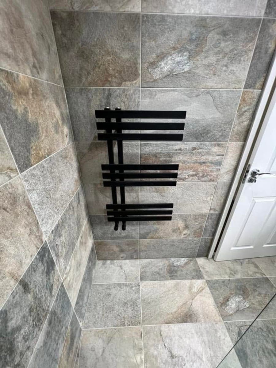 A matt black designer towel rail on slate tiling