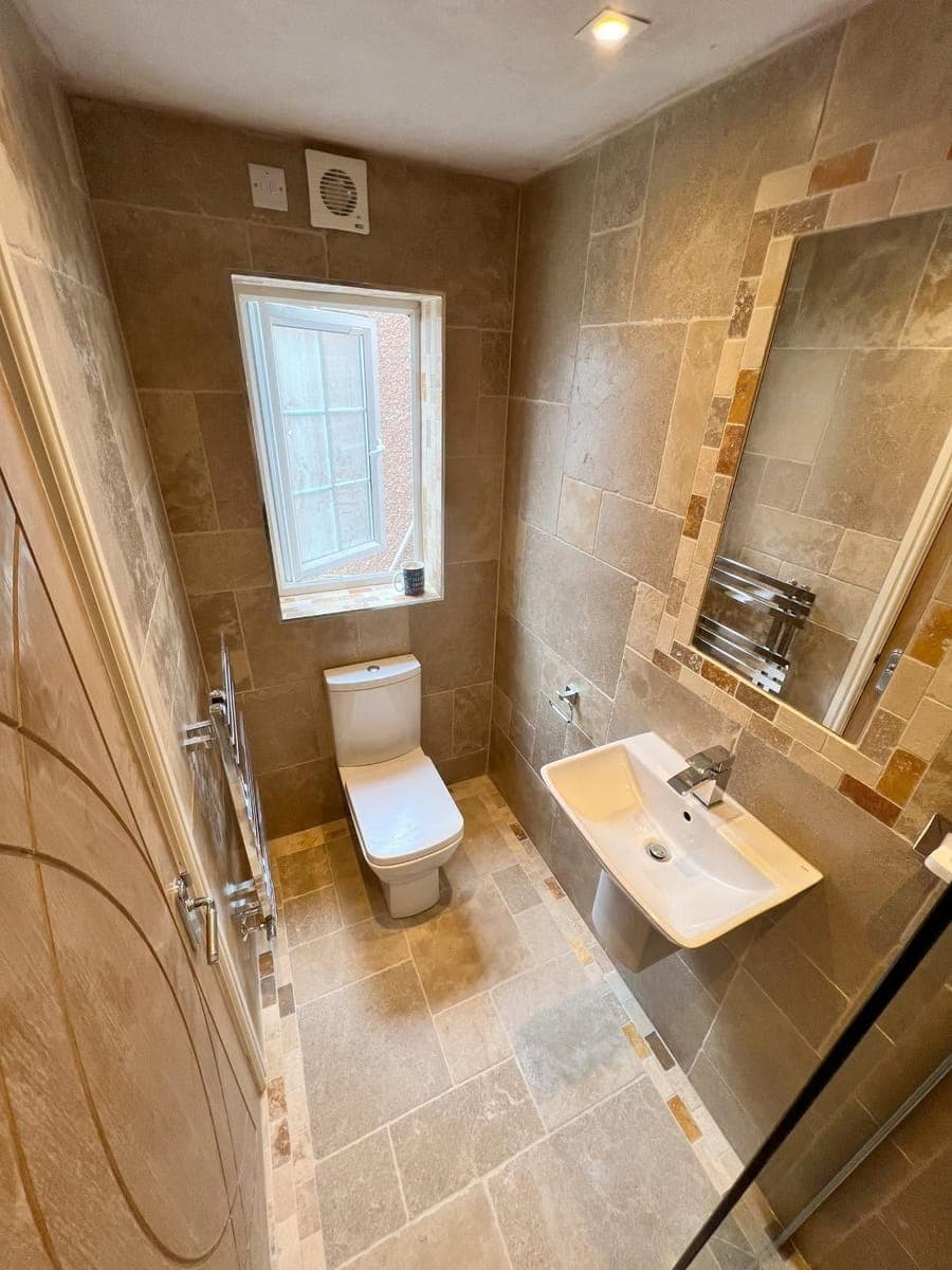 A travertine tiled cloakroom with a wall hung basin