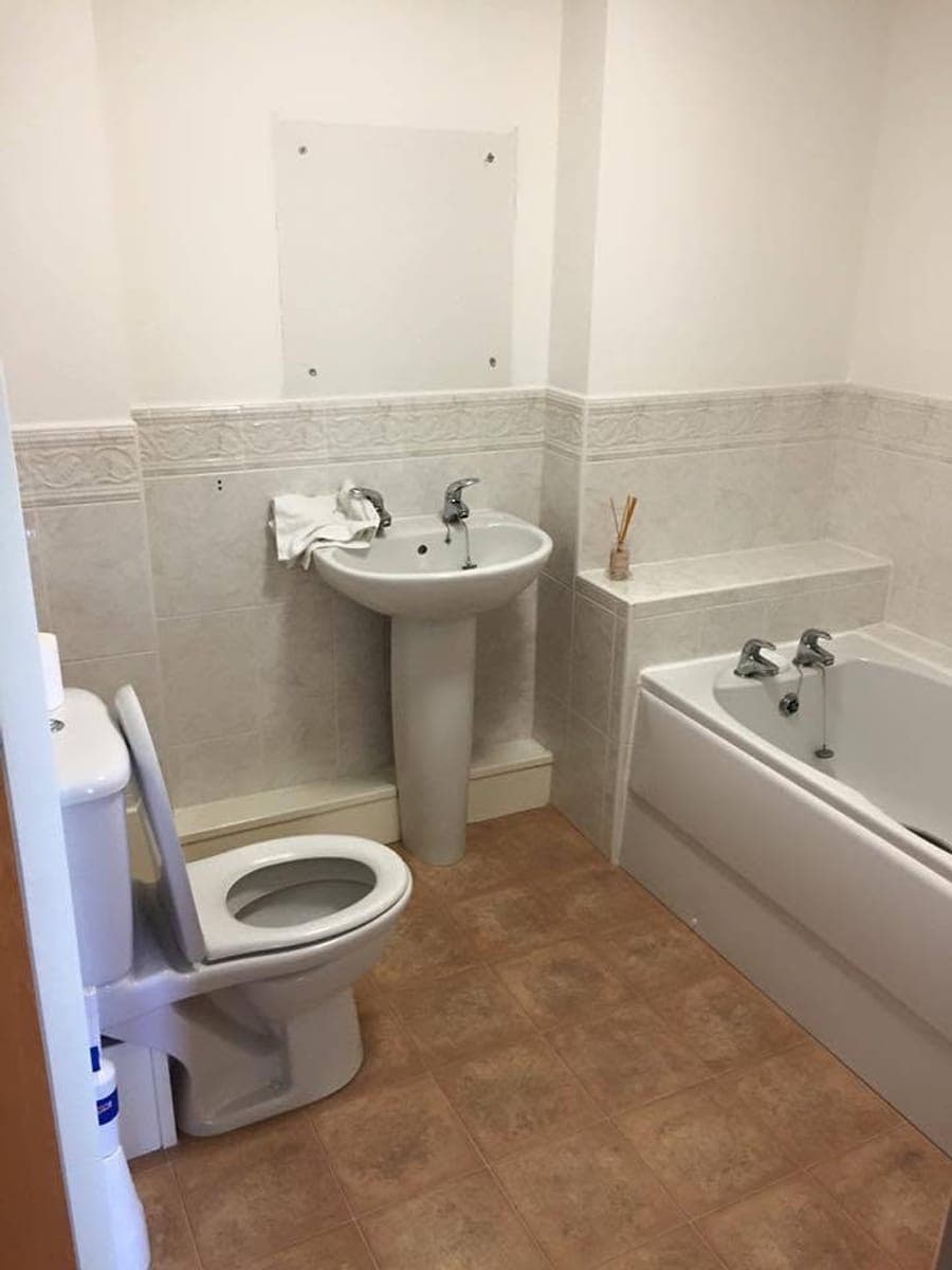 A dated bathroom with brown floor tiles, a pedestal basin and a boxed in bath